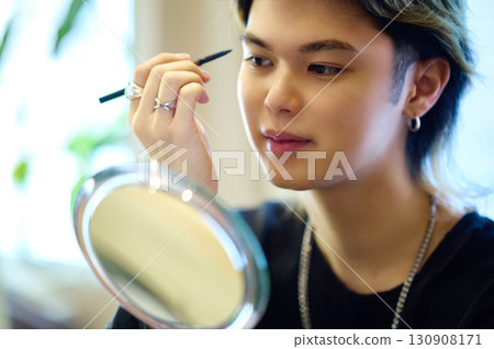 Men's beauty image of applying makeup while looking in a hand mirror 130908171