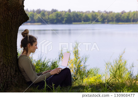 A Young Woman Enjoys Working Remotely by a Serene and Calm Lake During a Beautiful Day 130908477