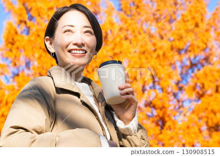 女人一邊喝熱飲一邊欣賞秋葉生活方式影像 130908515