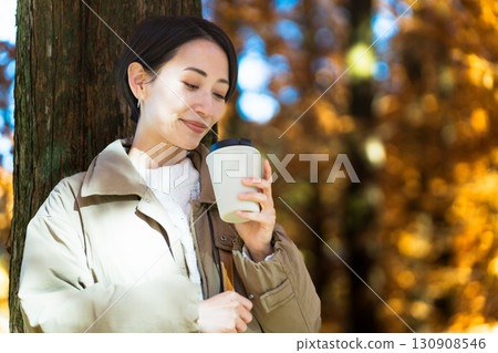 Woman drinking a hot drink while enjoying the autumn leaves Lifestyle image 130908546