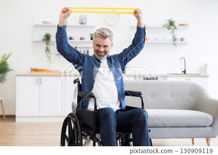 Mature Caucasian man in wheelchair performing stretching exercises with rubber resistance bands in a comfortable home kitchen environment, showcasing adaptability 130909119