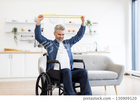 Mature Caucasian man sitting on wheelchair stretching rubber resistance band, engaging fitness exercise and promoting active living, located in modern and bright home 130909120