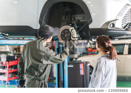 A female customer and a male mechanic receive an explanation about a car that has been lifted for a vehicle inspection 130909868