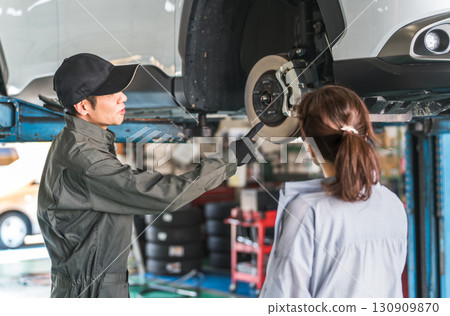 A female customer and a male mechanic receive an explanation about a car that has been lifted for a vehicle inspection A female customer and a male mechanic receive an explanation about a car that has been lifted for a vehicle inspection 130909870