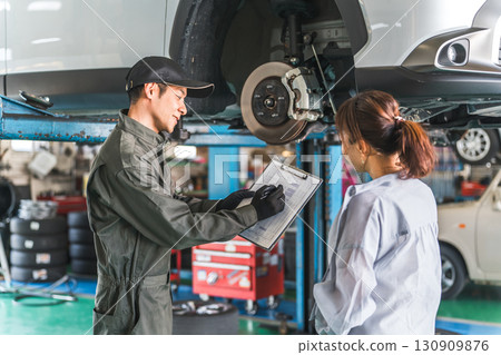 A female customer and a male mechanic receive an explanation about a car that has been lifted for a vehicle inspection 130909876