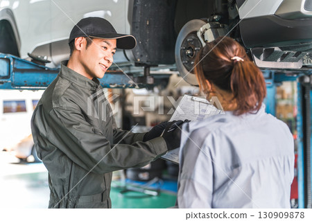 A female customer and a male mechanic receive an explanation about a car that has been lifted for a vehicle inspection 130909878