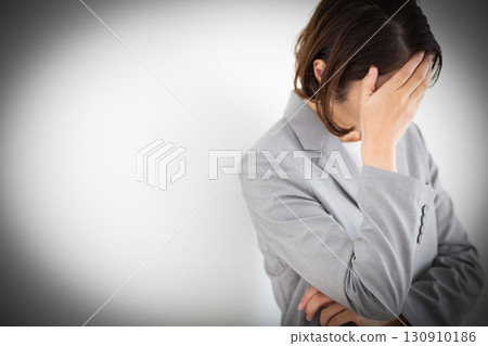 一位身穿灰色西裝的中年女商人抱著頭,憂心忡忡 一位身穿灰色西裝的中年女商人抱著頭,憂心忡忡 130910186