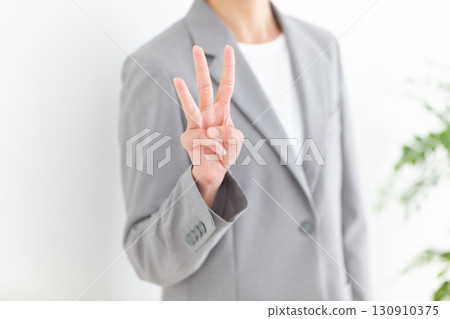A middle-aged female businesswoman in a gray suit holding up three fingers 130910375