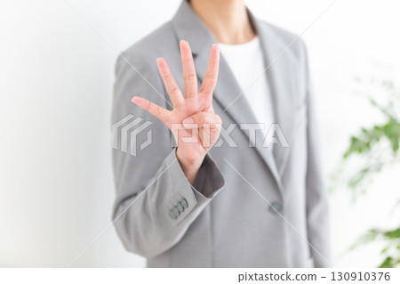 A middle-aged female businesswoman in a gray suit holding up four fingers 130910376