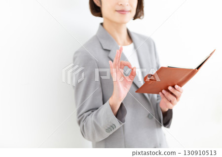 A middle-aged female business woman in a gray suit holding a notebook and signing a circle A middle-aged female business woman in a gray suit holding a notebook and signing a circle 130910513