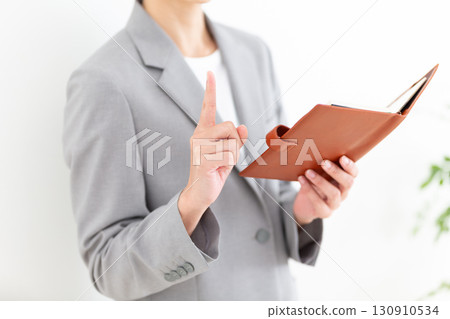 A middle-aged female businesswoman in a gray suit holding a notebook and pointing her index finger up A middle-aged female businesswoman in a gray suit holding a notebook and pointing her index finger up 130910534