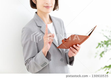 一位身穿灰色西裝的中年女商人手裡拿著筆記本，食指向上 130910535