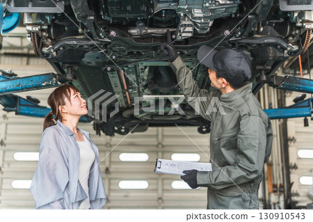 A female customer receives an explanation from a mechanic under the car 130910543