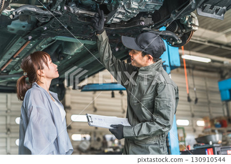 A female customer receives an explanation from a mechanic under the car A female customer receives an explanation from a mechanic under the car 130910544