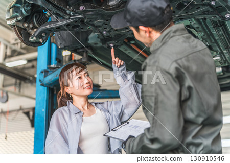 A female customer receives an explanation from a mechanic under the car 130910546