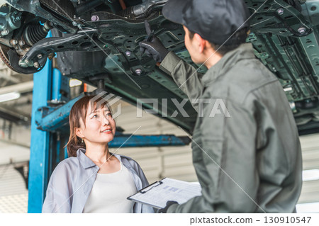 A female customer receives an explanation from a mechanic under the car 130910547