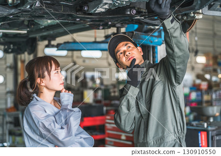A female customer receives an explanation from a mechanic under the car A female customer receives an explanation from a mechanic under the car 130910550