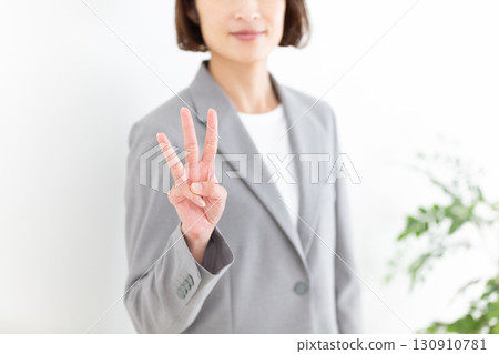A middle-aged female businesswoman in a gray suit holding up three fingers 130910781
