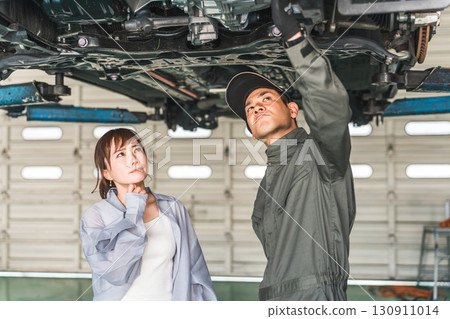 A female customer receives an explanation from a mechanic under the car 130911014
