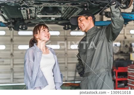 A female customer receives an explanation from a mechanic under the car A female customer receives an explanation from a mechanic under the car 130911018