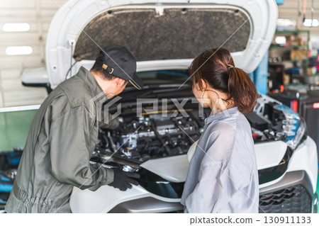 A mechanic explaining to a female customer in the car's engine room, a male mechanic staff member 130911133