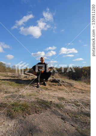Portrait of smiling caucasian artist plays wooden acoustic guitar in autumnal park. Young songwriter plays string musical instrument hobby outside in nature fall time. Audio music healing 130911280