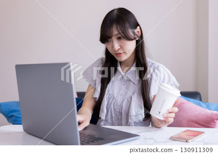 A Japanese woman with a serious expression working on a PC in the living room with a mug in her hand A Japanese woman with a serious expression working on a PC in the living room with a mug in her hand 130911309