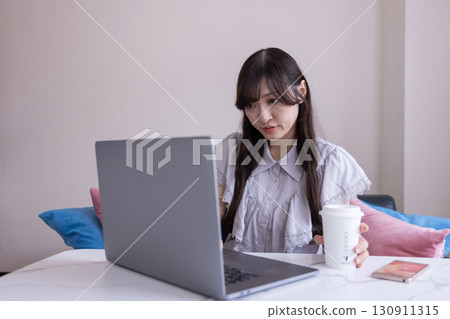 A Japanese woman with a serious expression working on a PC in the living room with a mug in her hand 130911315
