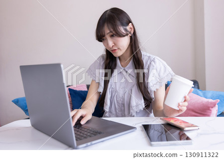 A Japanese woman with a serious expression working on a PC in the living room with a mug in her hand A Japanese woman with a serious expression working on a PC in the living room with a mug in her hand 130911322