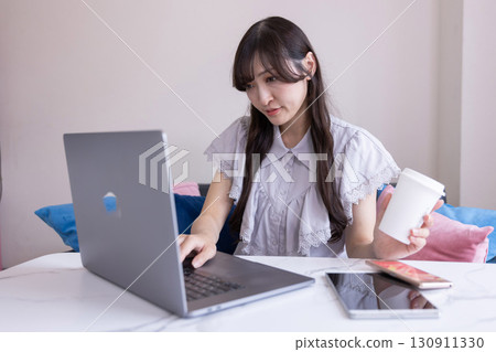 A Japanese woman with a serious expression working on a PC in the living room with a mug in her hand A Japanese woman with a serious expression working on a PC in the living room with a mug in her hand 130911330