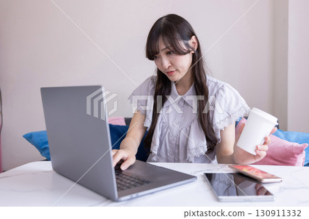 A Japanese woman with a serious expression working on a PC in the living room with a mug in her hand 130911332