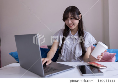 A Japanese woman with a serious expression working on a PC in the living room with a mug in her hand A Japanese woman with a serious expression working on a PC in the living room with a mug in her hand 130911343