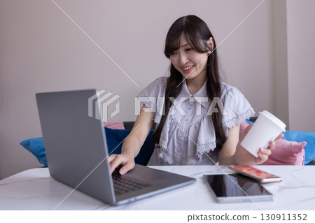 一位日本女性,表情嚴肅,手裡拿著杯子,在客廳使用電腦 一位日本女性,表情嚴肅,手裡拿著杯子,在客廳使用電腦 130911352