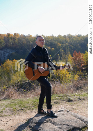 Beautiful blonde man playing acoustic guitar and singing relaxing enjoying outdoors on sunny autumn day. Artist learning and practicing playing musical instrument. Fall leaves autumnal Beautiful blonde man playing acoustic guitar and singing relaxing enjoying outdoors on sunny autumn day. Artist learning and practicing playing musical instrument. Fall leaves autumnal 130911362