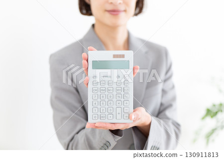 一位身穿灰色西裝、手裡拿著計算機的中年女商人 一位身穿灰色西裝、手裡拿著計算機的中年女商人 130911813