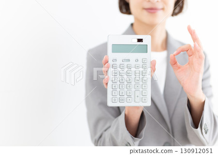 A middle-aged female business woman in a gray suit holding a calculator and making a circle sign A middle-aged female business woman in a gray suit holding a calculator and making a circle sign 130912051