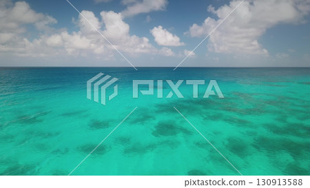 Breathtaking aerial view of transparent turquoise water gently merging with deep blue ocean under a partially cloudy sky, creating a mesmerizing seascape. Travel background, idyllic exotic paradise 130913588