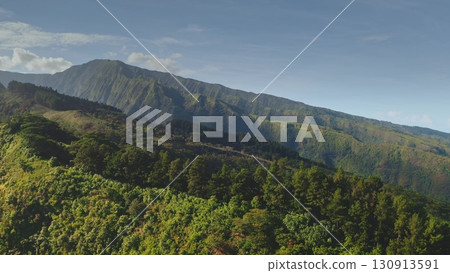Aerial drone captures a breathtaking view of a lush green mountain range, its slopes densely covered in tropical vegetation, creating a stunning natural landscape 130913591