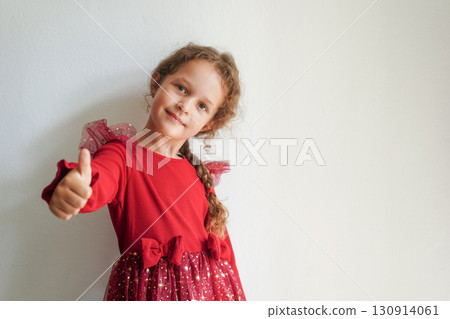 A cheerful girl in a sparkly red dress gives a thumbs up and smiles confidently 130914061