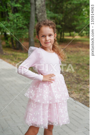 A smiling girl in a pink ruffled dress strikes a sideways pose with her hand on her hip near a forest path. A smiling girl in a pink ruffled dress strikes a sideways pose with her hand on her hip near a forest path. 130914063