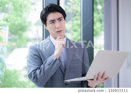 A man in a suit with a laptop, a consultant, or a salesman, thinking while looking at the screen 130915511