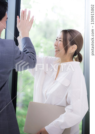 Two smiling businessmen celebrating success and achievements with a high five. Positive men and women celebrating project success Two smiling businessmen celebrating success and achievements with a high five. Positive men and women celebrating project success 130915802