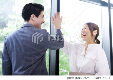 兩位面帶微笑的商人擊掌慶祝成功和成就。積極向上的男士和女士慶祝項目成功 兩位面帶微笑的商人擊掌慶祝成功和成就。積極向上的男士和女士慶祝項目成功 130915804