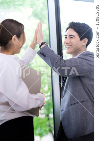 Two smiling businessmen celebrating success and achievements with a high five. Positive men and women celebrating project success Two smiling businessmen celebrating success and achievements with a high five. Positive men and women celebrating project success 130915805