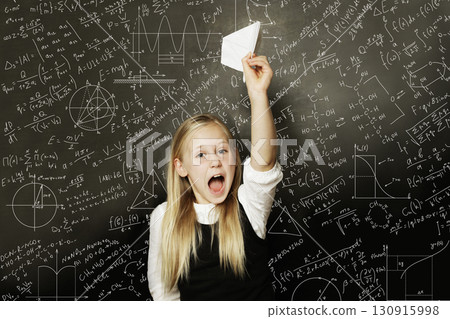 Playful school child girl standing in classroom on blackboard background. Education concept Playful school child girl standing in classroom on blackboard background. Education concept 130915998