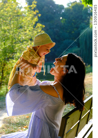 Mother Lifting Baby Outdoors in Sunny Park 130916485