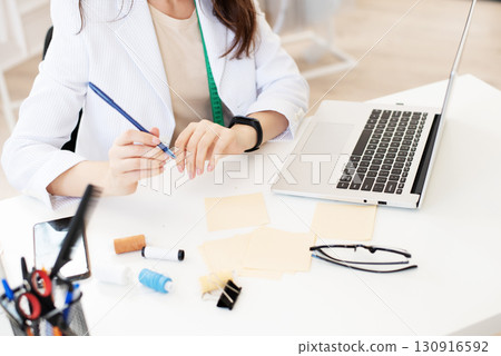 A person using a laptop at a messy desk with various craft supplies. This image represents creative work, design 130916592