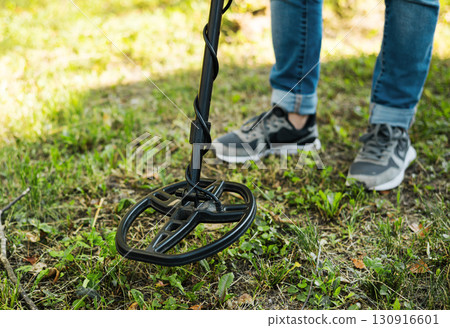 An explorer using a metal detector to search for treasure or artifacts in a grassy field. An explorer using a metal detector to search for treasure or artifacts in a grassy field. 130916601