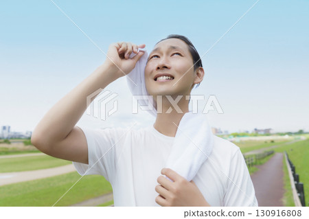Young man wiping sweat with a towel while running 130916808