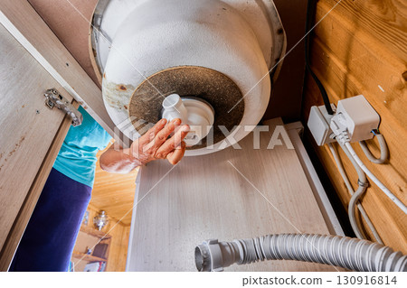 Bottle trap inlet pipe is being installed by plumber hand under sink bottom aligned with circular opening of basin. 130916814